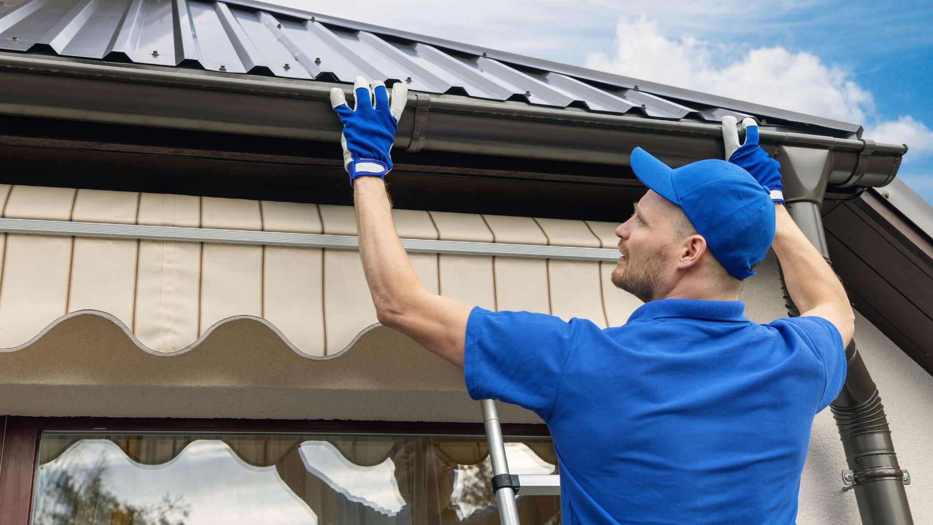 Worker in blue uniform installing or repairing roof gutters