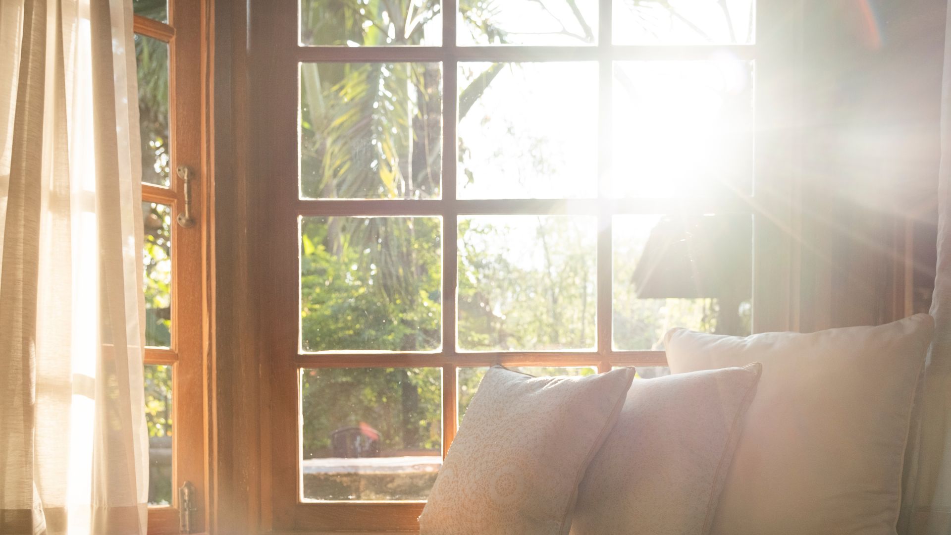 Sunlight streaming through wooden windows with soft curtains and pillows