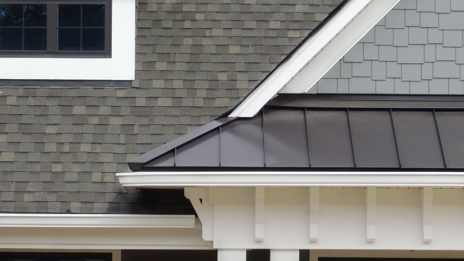Close-up of house roof with gray shingles, white trim, and metal roofing
